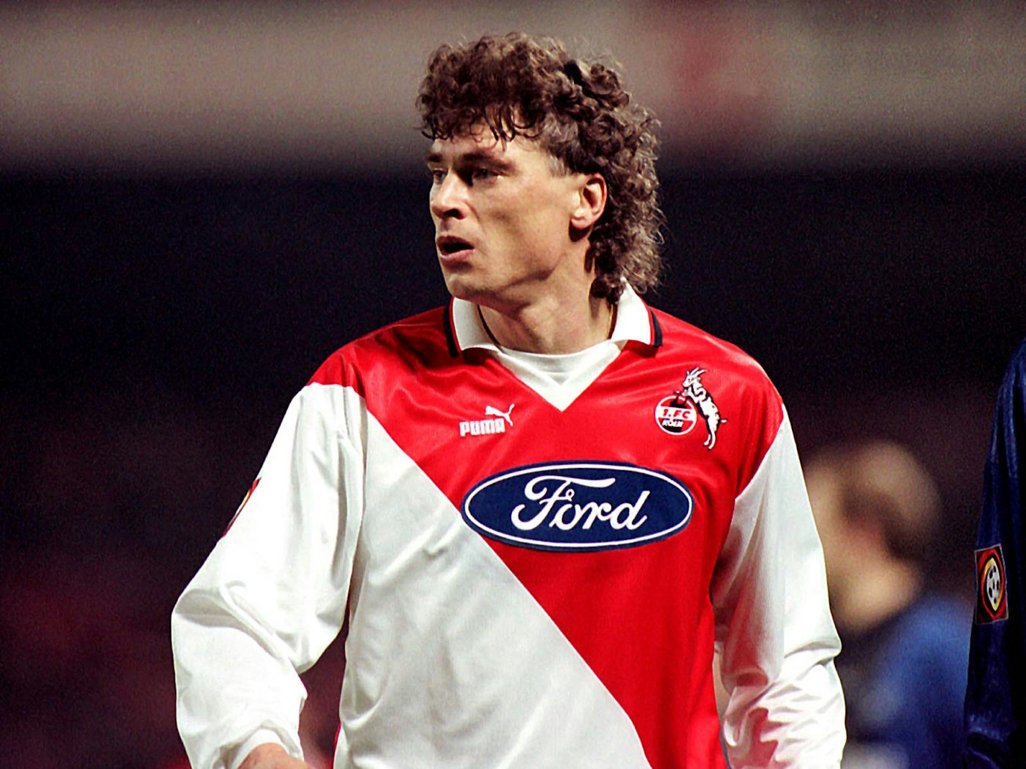 Toni Polster ist fokussiert. Er trägt ein rot-weißes Köln-Trikot von Puma mit dem Ford-Logo auf der Brust.